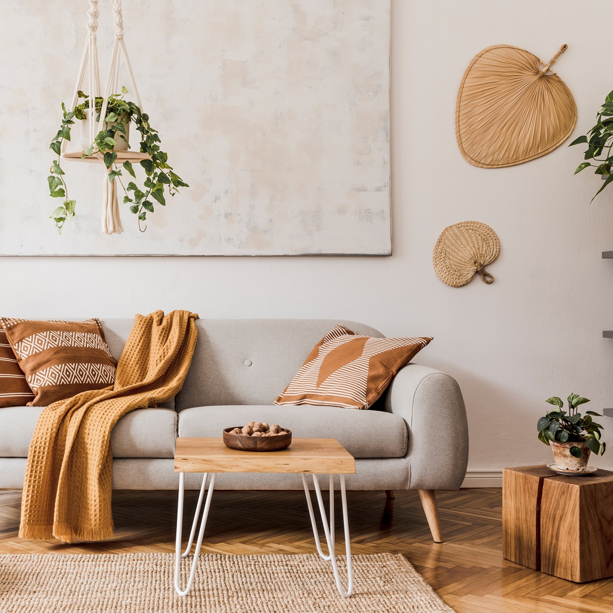 Stylish composition of creative and cozy living room interior with grey sofa, coffee table, plants, carpet and beautiful accessories. White walls and parquet floor.